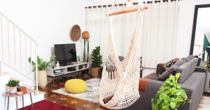 Sala de TV, com destaque para um pufe amarelo de tricô no centro do ambiente, uma rede cadeira trançada e o tapete pirâmides da MinD. 
