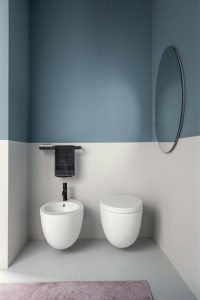 Banheiro com um accent wall na cor vintage blue, a parte inferior da parede é branca e a superior é azul. Há também um espelho redondo na parede.